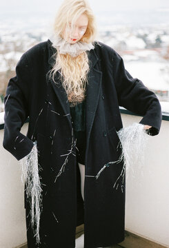 Woman in a long black coat displaying tinsel decorations 