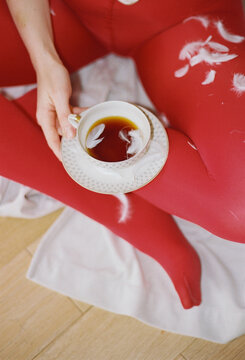 Woman in red tights holding a cup of tea with feathers 