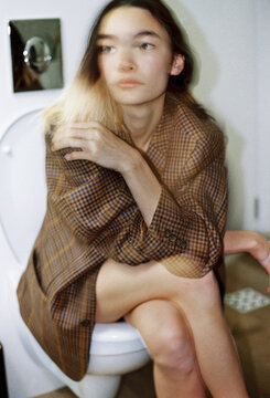 Young woman sitting on toilet in casual outfit
