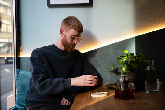 Young man drinking tea in cafe by window sunlight
