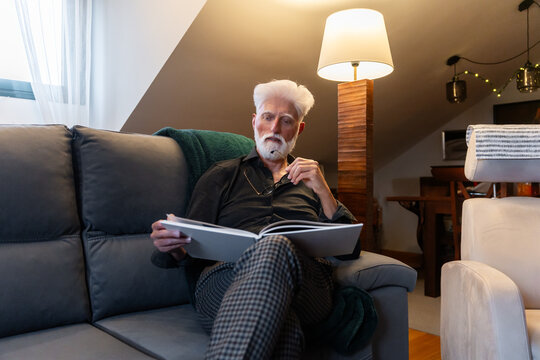 Elderly Man Reading Book On Couch