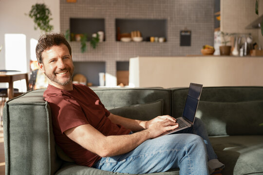 Cheerful man using laptop and looking at camera