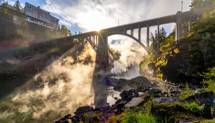 Majestic waterfall cascading under a bridge with sunbeams piercing through.