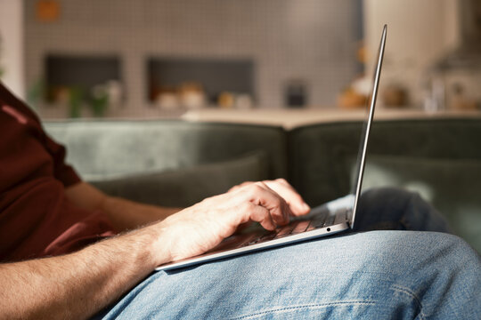 Crop of anonymous man using laptop at home