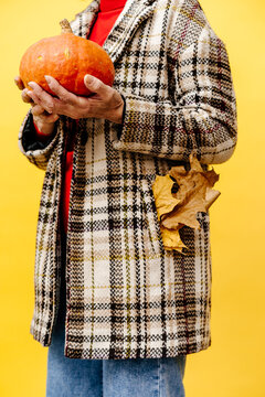 Woman in Plaid Coat Holding Pumpkin with Autumn Leaves in Pocket