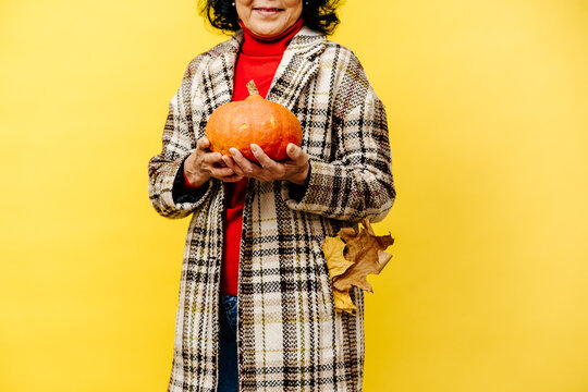 Senior Woman in Overcoat Holding Pumpkin, Autumn Leaves in Pocket