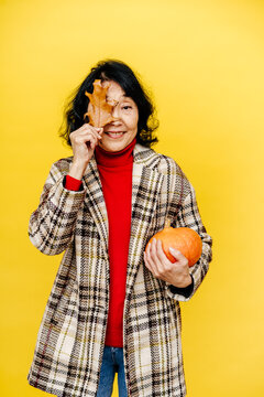 Woman Holding Pumpkin and Hiding Eye Behind Autumn Leaf