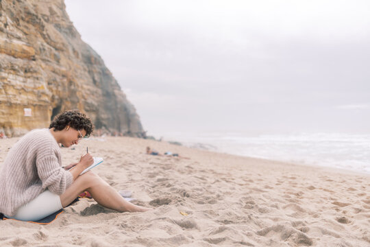 Artist Writing on a Watercolor Postcard While Sitting on the Beach