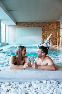 Happy couple enjoying champagne in thermal spa resort pool