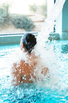 Man relaxing under waterfall in thermal spa pool