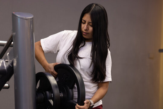 Young woman adding weights to a machine in a modern gym, engaging in a focused workout session to build strength and improve overall physical fitness and health