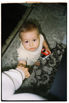 Child plays with a toy car while reaching for an adult's hand 