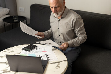Man reviewing utility bills and financial statements on a laptop at home