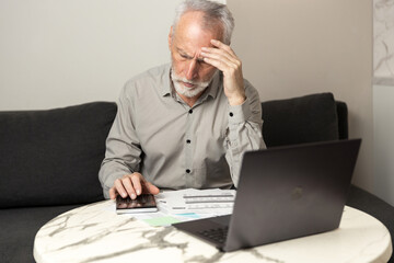 Man calculates expenses and reviews bills while sitting at home with a laptop