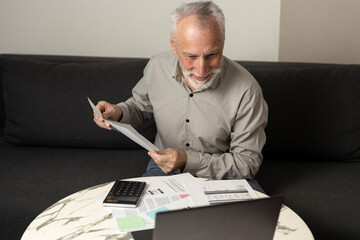 Man reviewing bills and statements while using a laptop in a living room