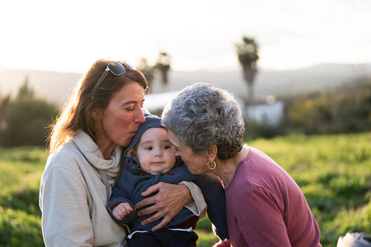 Mother and grandmother kissing baby grandson