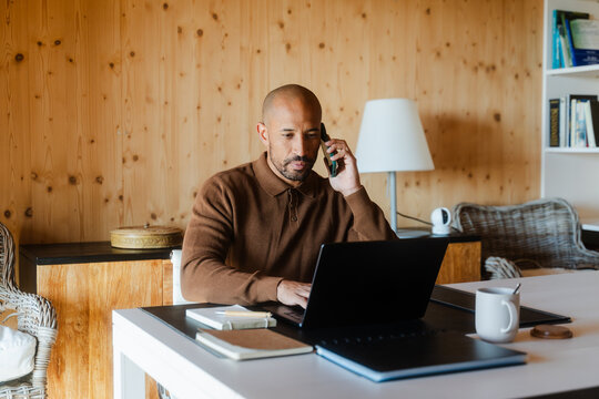 Focused Businessman Multitasking on Phone and Laptop at Office Desk