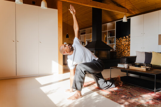 Bald Man Practicing Revolved High Lunge Yoga Pose on Sunny Day at Home