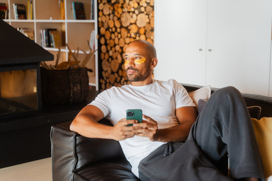 Relaxing with Collagen Patches: Bald Man Unwinds on Sofa at Home