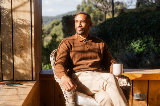 Man Relaxing with Tea on Log Cabin Balcony, Enjoying Sunny Day