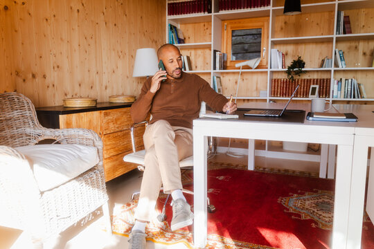 Businessman Talking on Smartphone and Taking Notes in Sunlit Office