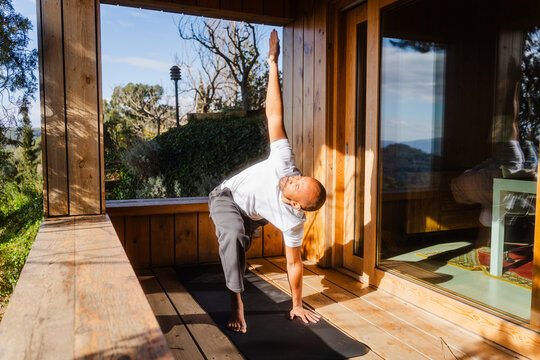 Bald Man Practicing Revolved High Lunge Pose on Sunny Day at Log Cabin