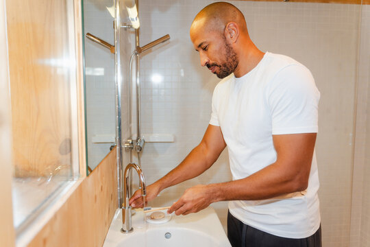 Man Rinsing Toothbrush Under Sink in Home Bathroom