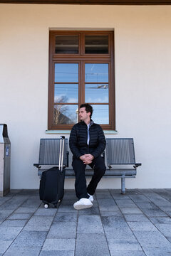 Man with a suitcase waiting for a train at a stop on a sunny day.