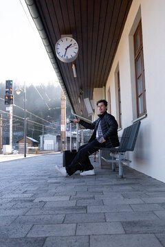 Man with a suitcase waiting for a train at a stop on a sunny day.