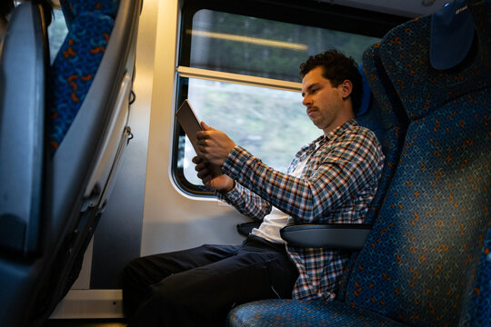 Man sits in train with tablet.