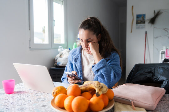 Bored woman using smartphone and laptop at home