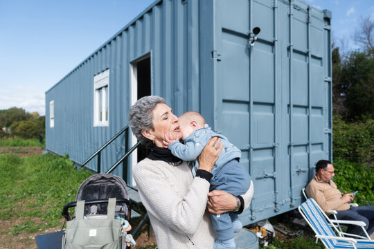 Grandmother holding her grandson in front of a container house
