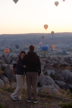 A young couple stands against a backdrop of rising hot air balloons.