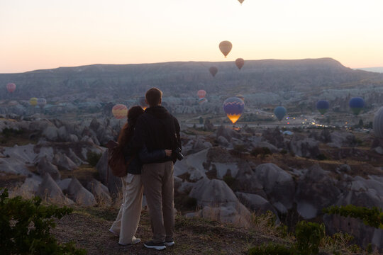 A young couple stands against a backdrop of rising hot air balloons.
