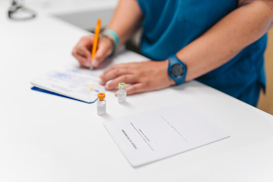 Doctor compiling medical record with vaccine and prescription on desk