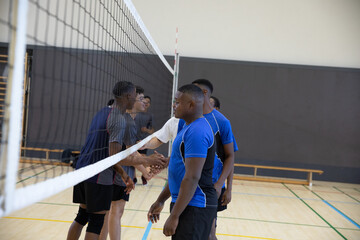 African American teen boys exchanging handshakes on gym court by net, wearing jerseys, copy space