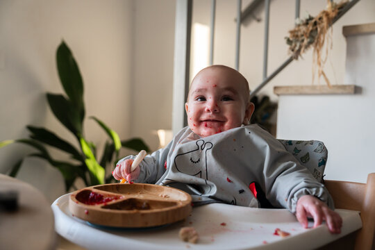 Smiling baby enjoying meal in high chair wearing bib