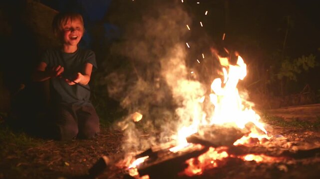Cute boy is roasting marshmallows on a bonfire on a summer evening. School age child with smores at camp fire. Outdoor summer and autumn fun during holidays for family with kids in countryside.Camping