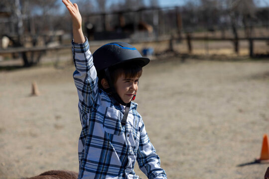 A child raises one hand while riding a horse in an outdoor setting