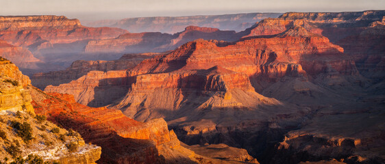 Breathtaking panoramic landscape of the Grand Canyon National Park in Arizona during a vibrant sunset. Majestic red rock formations, deep shadows, and golden light over the vast desert canyon.