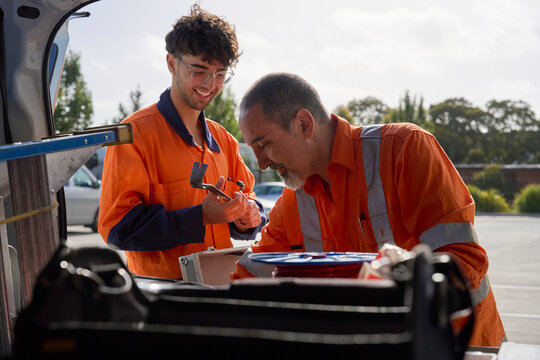 Two workers organize tools and materials in a vehicle at work site