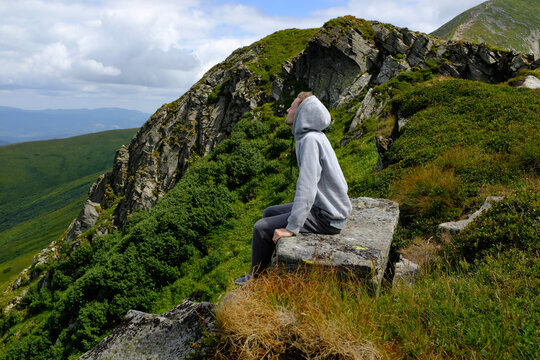 Young man sitting on a rock looking at green mountain valley