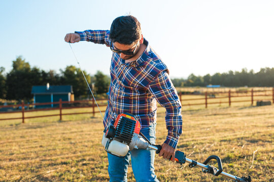 Farmer starting brushcutter in farm field