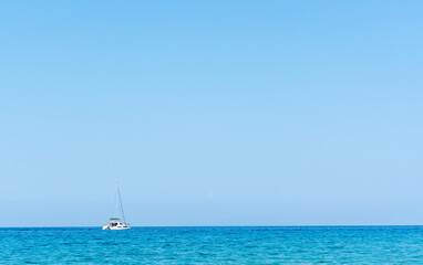 Fototapeta premium Lone white sailboat anchored on vast calm turquoise Adriatic sea under clear bright blue sky with minimalist horizon. Concept of freedom, solitude, luxury sailing vacation and Mediterranean serenity.