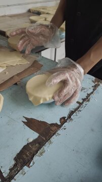 
Close-up of hands wearing protective gloves putting and arranging puff pastry lids on top of bowls of zuppa soup before baking in the oven.