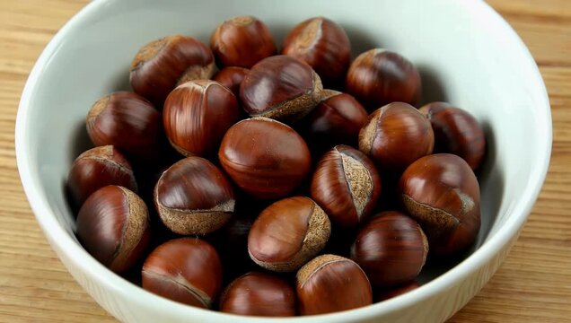 rustic 4K food close up featuring collection of fresh organic chestnuts distinguished by ir smooth brown shells neatly arranged in ceramic bowl captured in close up view against textured wooden