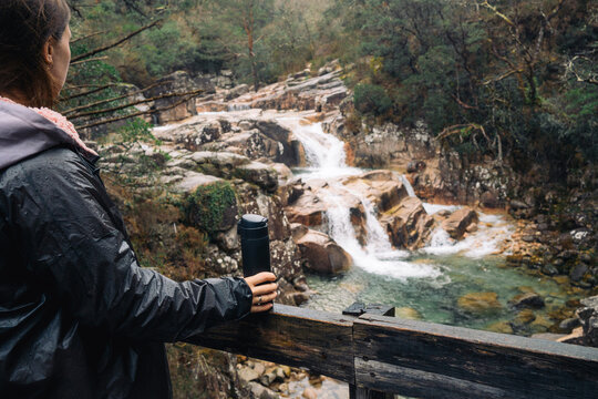 Person enjoying a scenic waterfall view with a thermos in hand