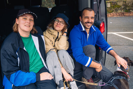 Smiling friends sitting in the back of a van with a dog