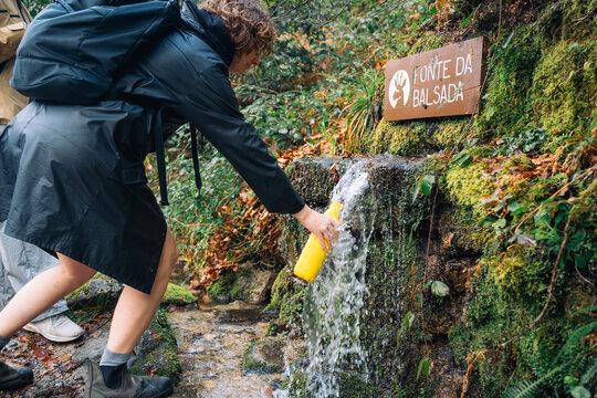 Person filling bottle from natural spring waterfall