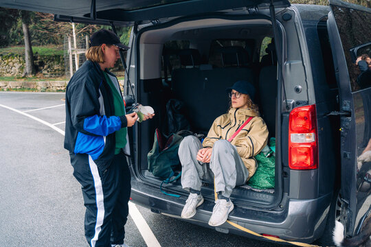Person sitting in the back of a van while another stands nearby